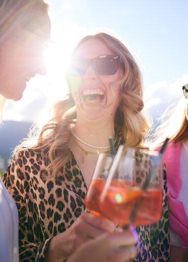 Three smiling women at a summer lounge event in Kleinwalsertal, enjoying rosé drinks in the sunlight. | © Kleinwalsertal Tourismus eGen • Photographer: Oliver Farys