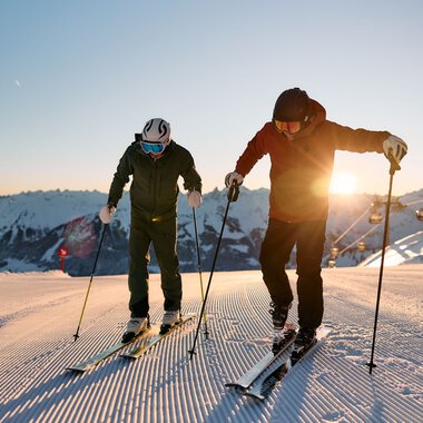 Two skiers at sunrise on a snowy slope in Kleinwalsertal, Alps, winter 2024. | © Kleinwalsertal Tourismus eGen • Photographer: Oliver Farys