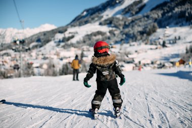 Ein Kind beim Skifahren auf einer Piste im Schnee, umgeben von Bergen und anderen Skifahrern, in winterlicher Landschaft. | © Kleinwalsertal Tourismus eGen • Fotograf: Oliver Farys