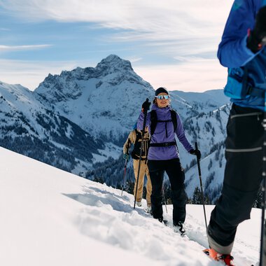 Group of skitourers trekking through snowy mountain landscape in Kleinwalsertal, equipped with backpacks and ski poles. | © Kleinwalsertal Tourismus eGen • Photographer: Oliver Farys