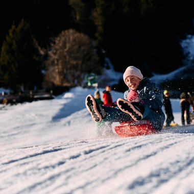 A child sledding down a snowy hill, enjoying winter fun in Kleinwalsertal. | © Kleinwalsertal Tourismus eGen • Photographer: Oliver Farys