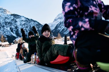 Kinder beim Rodeln im Schnee in den Bergen, lachend und spielend, Winterurlaub im Kleinwalsertal. | © Kleinwalsertal Tourismus eGen • Fotograf: Oliver Farys