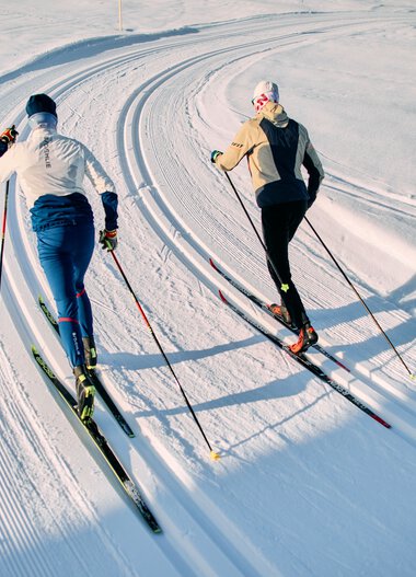 Two cross-country skiers in classic style on a snow-covered trail in Kleinwalsertal, Schwarzwasserloipe, during the winter 2025 season. | © Kleinwalsertal Tourismus eGen • Photographer: Oliver Farys