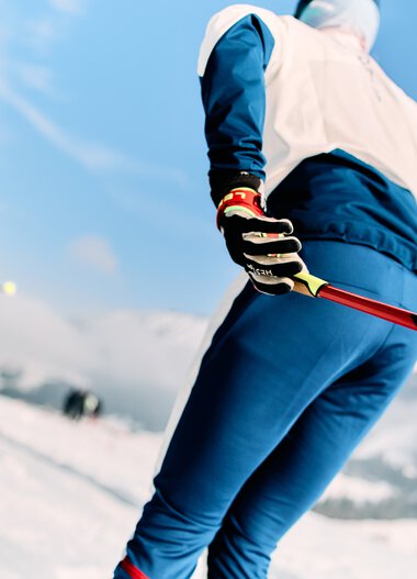 Cross-country skiers in a snowy landscape with mountains and blue sky in the background | © Kleinwalsertal Tourismus eGen • Photographer: Oliver Farys