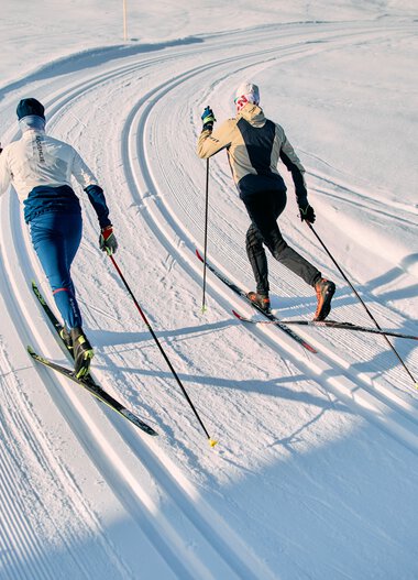 Two cross-country skiers on the Schwarzwasserloipe trail in Kleinwalsertal, gliding through a sunny winter landscape. | © Kleinwalsertal Tourismus eGen • Photographer: Oliver Farys