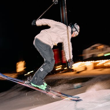 Skifahrer bei Nacht im Kleinwalsertal, beim Nachtskifahren unter Flutlicht, mit Bewegungsschärfe und nächtlicher Bergenszenerie im Hintergrund. | © Kleinwalsertal Tourismus eGen • Fotograf: Oliver Farys