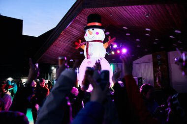 Large snowman decoration at a winter event in Kleinwalsertal, surrounded by children celebrating the snow festival. | © Kleinwalsertal Tourismus eGen • Photographer: Oliver Farys