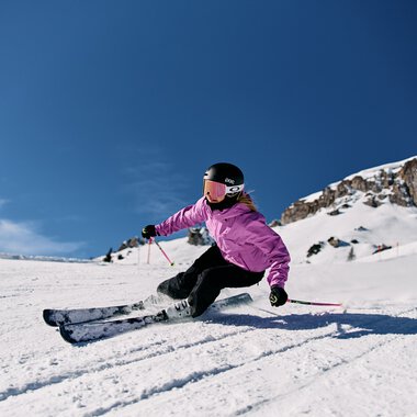 Girl skiing in the snow in the Alps, wearing a helmet and pink jacket on a sunny winter day. | © Kleinwalsertal Tourismus eGen • Photographer: Oliver Farys