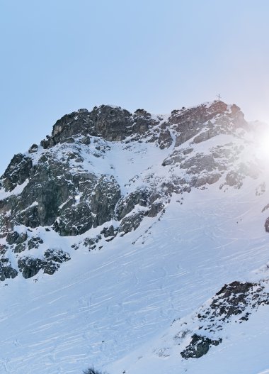 Schneebedeckte Berge in den Alpen bei Sonnenschein, Blick auf eine felsige Gipfelregion im Winter. | © Kleinwalsertal Tourismus eGen • Fotograf: Oliver Farys