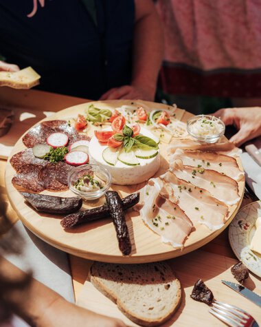 Mountain picnic with cheese, sausage, bread, and cold cuts during an outdoor hiking day. | © Kleinwalsertal Tourismus eGen • Photographer: Stefan Klauser