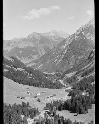 Schöne Berglandschaft im Tal mit kleinen Bauernhöfen, umgeben von hohen Gipfeln, im historischen Schwarz-Weiß-Foto. | © Kleinwalsertal Tourismus eGen • Karl Max Kessler Archiv