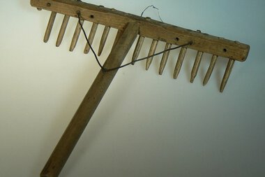 A wooden rake with long nails, likely used in historical agriculture. It has a handle and is attached with a wire. | © Kleinwalsertal Tourismus eGen • Stefan Heim