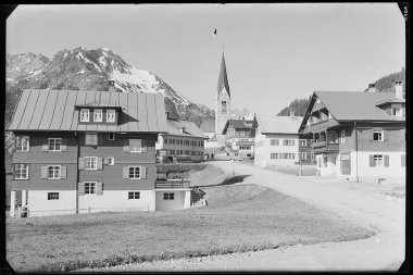 Historisches Schwarz-Weiß-Foto des Dorfes Mittelberg mit Kirche und Bergen im Hintergrund. | © Kleinwalsertal Tourismus eGen • Karl Max Kessler Archiv