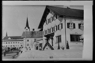 Historisches Schwarz-Weiß-Foto eines Schuh- und Modehauses im Zentrum von Riezlern, mit einem Mann und einer Frau vor dem Geschäft, im Schnee. | © Kleinwalsertal Tourismus eGen • Karl Max Kessler Archiv