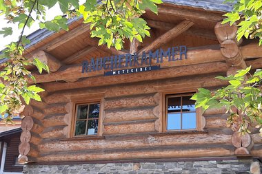 Wooden building with two small windows, likely a smoke chamber, surrounded by green leaves. | © Kleinwalsertal Tourismus eGen • Räucherkammer