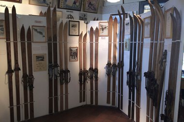 Ski Museum mit alten Skiern, die an einer weißen Trennwand montiert sind, im Walserhaus. | © Kleinwalsertal Tourismus eGen