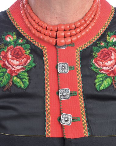 Close-up of a traditional costume's back, featuring red and black elements, embroidery, buttons, and a red necklace. | © Kleinwalsertal Tourismus eGen • Photographer: Christoffer Leitner
