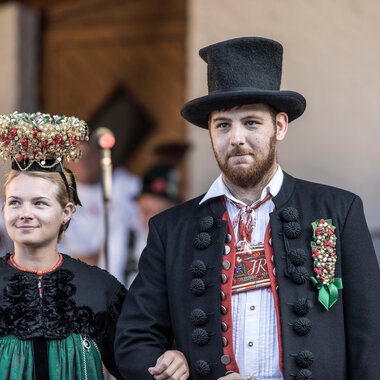Ein Mann und eine Frau in traditionellen Trachten bei einem Alphornfestival, die Frau trägt einen Blumenkranz auf dem Kopf. | © Kleinwalsertal Tourismus eGen • Fotograf: Frank Drechsel
