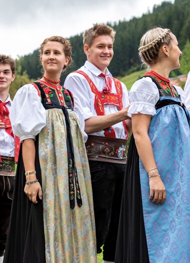 Group of people in traditional costumes at the Alphorn festival outdoors with mountains in the background. | © Kleinwalsertal Tourismus eGen • Photographer: Frank Drechsel