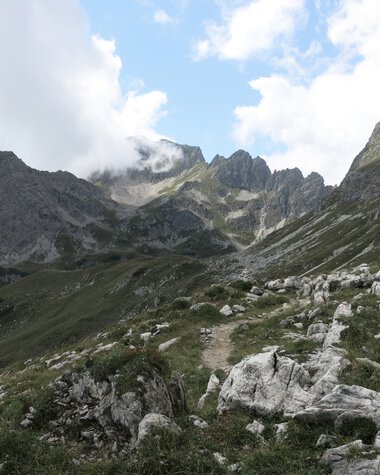 Mountain landscape with peaks, rocks, and green areas under a partly cloudy sky. | © Kleinwalsertal Tourismus eGen • Photographer: Antje Pabst