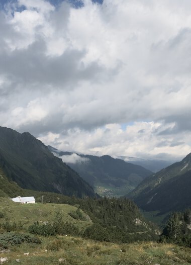 Mountain landscape with valley, cloudy sky, and green hills in the mountains. | © Kleinwalsertal Tourismus eGen • Photographer: Antje Pabst