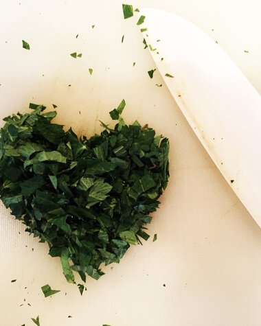 Chopped herbs arranged in a heart shape on a cutting board, with a knife beside them. | © Kleinwalsertal Tourismus eGen