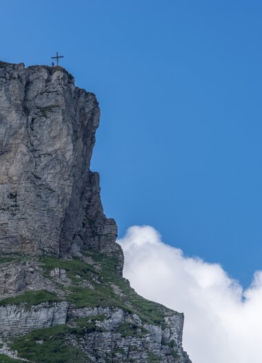 Felsen am Gipfel des Ifen mit Gipfelkreuz vor blauem Himmel und Wolken im Sommer. | © Kleinwalsertal Tourismus eGen • Fotograf: Steffen Berschin