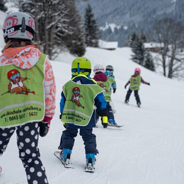 Kinder im Skikurs lernen das Skifahren auf einer verschneiten Piste mit Skilehrern und Eltern in Mittberg. | © Skischule Mittelberg