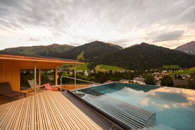 Panoramaaufnahme eines Hotel-Pools auf einer Deckterrasse mit Blick auf Berge und grüne Landschaft bei Sonnenuntergang. | © Hotel Erlebach