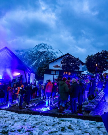 People gather at an Alpine horn festival in a snowy mountain setting during nighttime with blue lighting. | © Kleinwalsertal Tourismus eGen • Photographer: Frank Drechsel